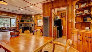 Een houten interieur met een eettafel, stoelen, een open haard, een keukenhoek en een wand van natuursteen.