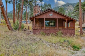 A rustic cabin with a stone chimney, wooden exterior, and large windows.