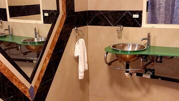 Ein Badezimmer mit einem großen Spiegel, einem Waschbecken mit grüner Ablage, einer Toilette und einem gemusterten Boden.