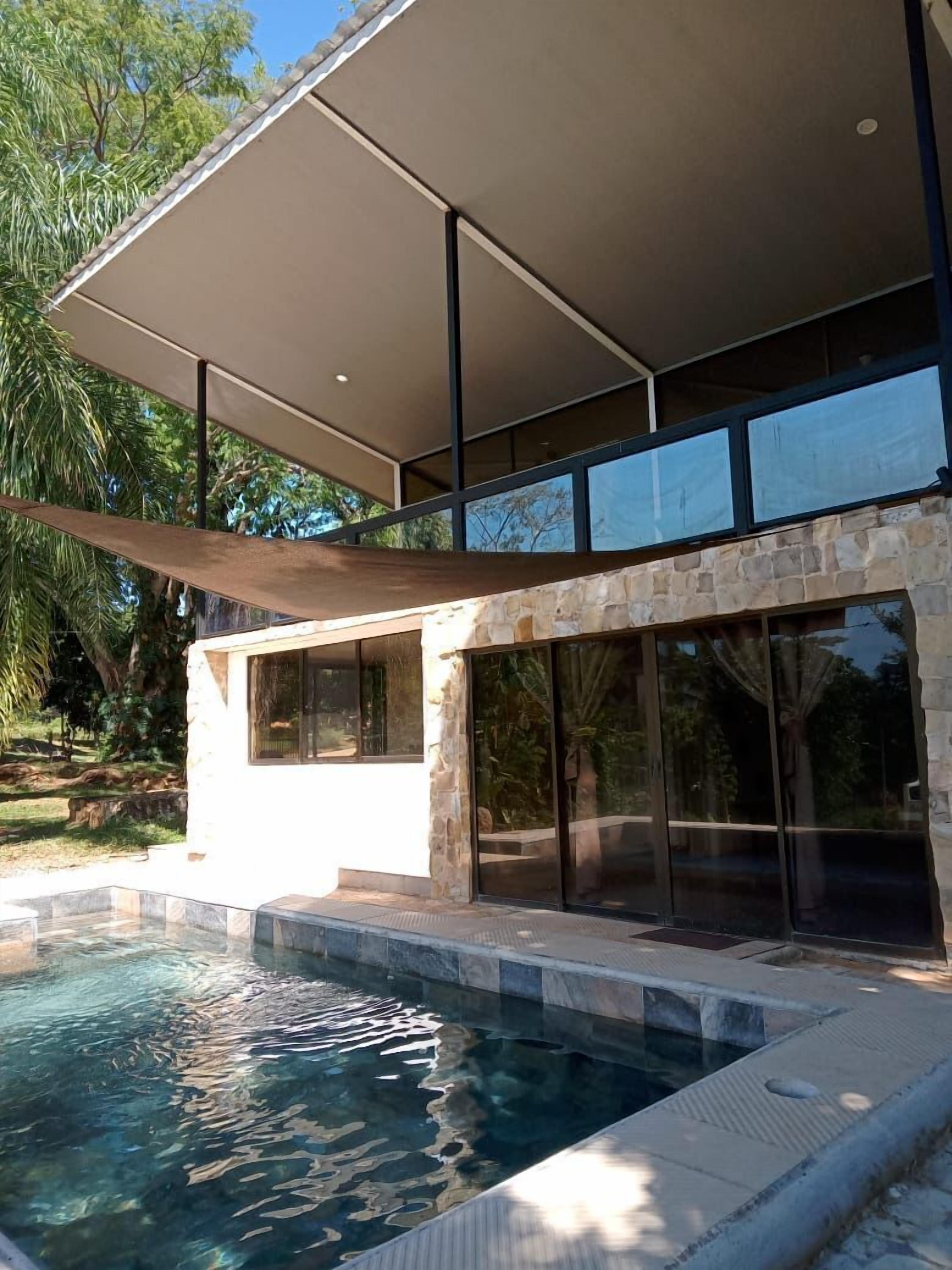 A modern house with a swimming pool, stone exterior, large windows, and a covered patio area.