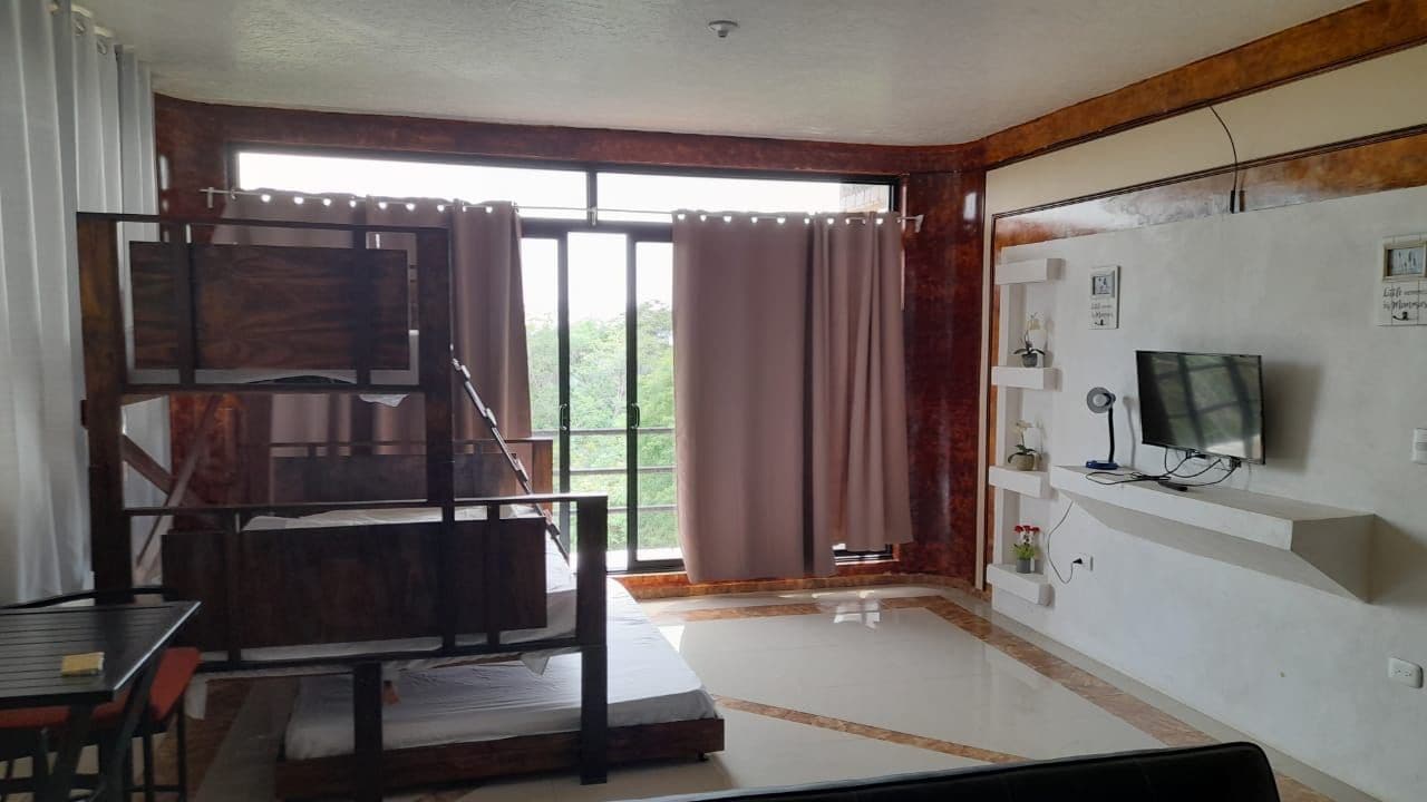 Une chambre avec un lit, une télévision, un bureau et une fenêtre avec des rideaux.