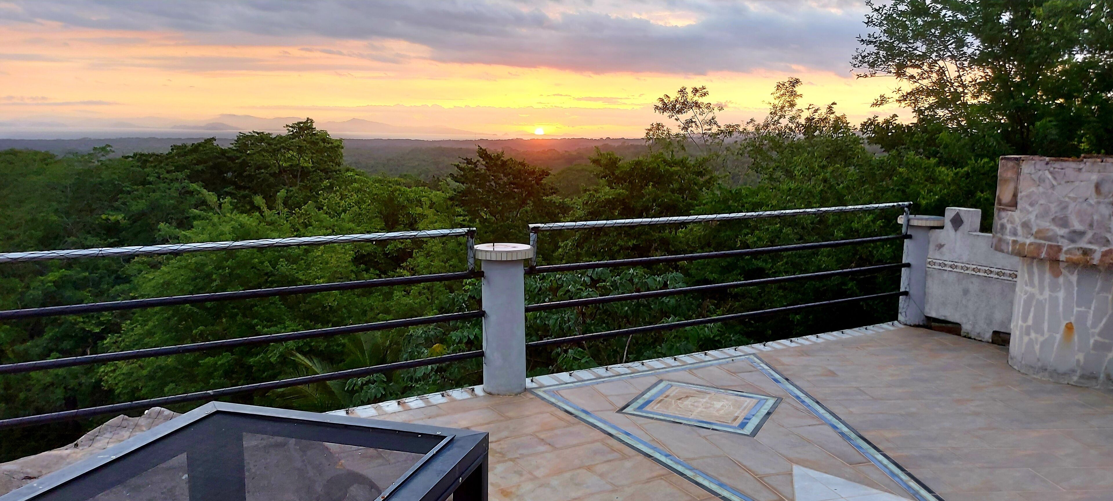Une terrasse offrant une vue sur le coucher de soleil au-dessus d’un paysage boisé.