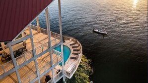 A poolside area with a circular seating arrangement and a boat on the water. - Allie's - Amazing 8,000 SF Home with --Private Pool--hot tub-- Sleeps 26+  (Sunrise Beach)
