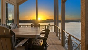 A covered outdoor dining area with a table and chairs, overlooking a body of water and a sunset. - Allie's - Amazing 8,000 SF Home with --Private Pool--hot tub-- Sleeps 26+  (Sunrise Beach)