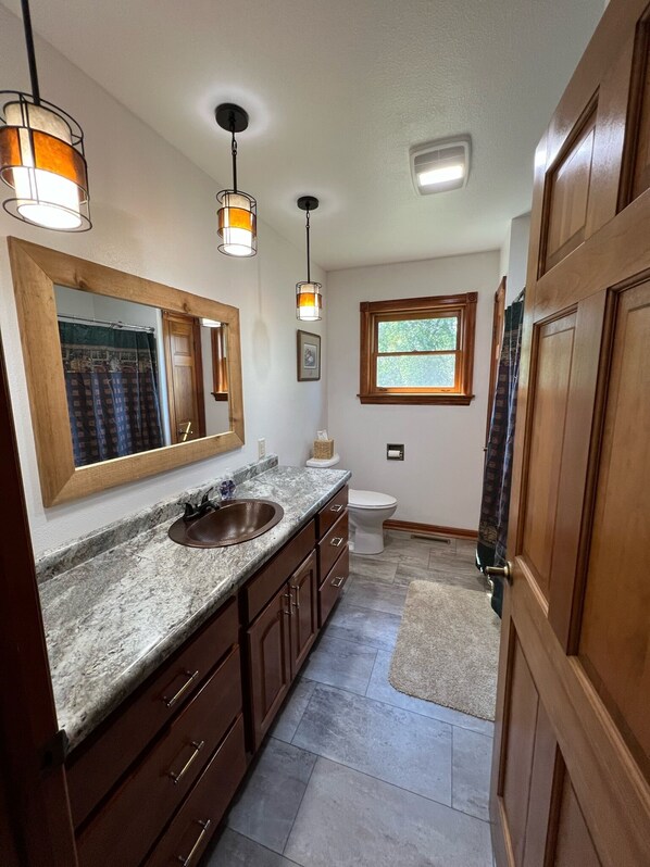 A modern bathroom with a large vanity, a sink, and a toilet. There are pendant lights above the vanity and a window providing natural light.