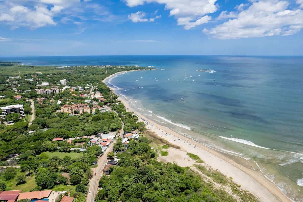 An aerial view of a coastal area with a beach, buildings, and boats.