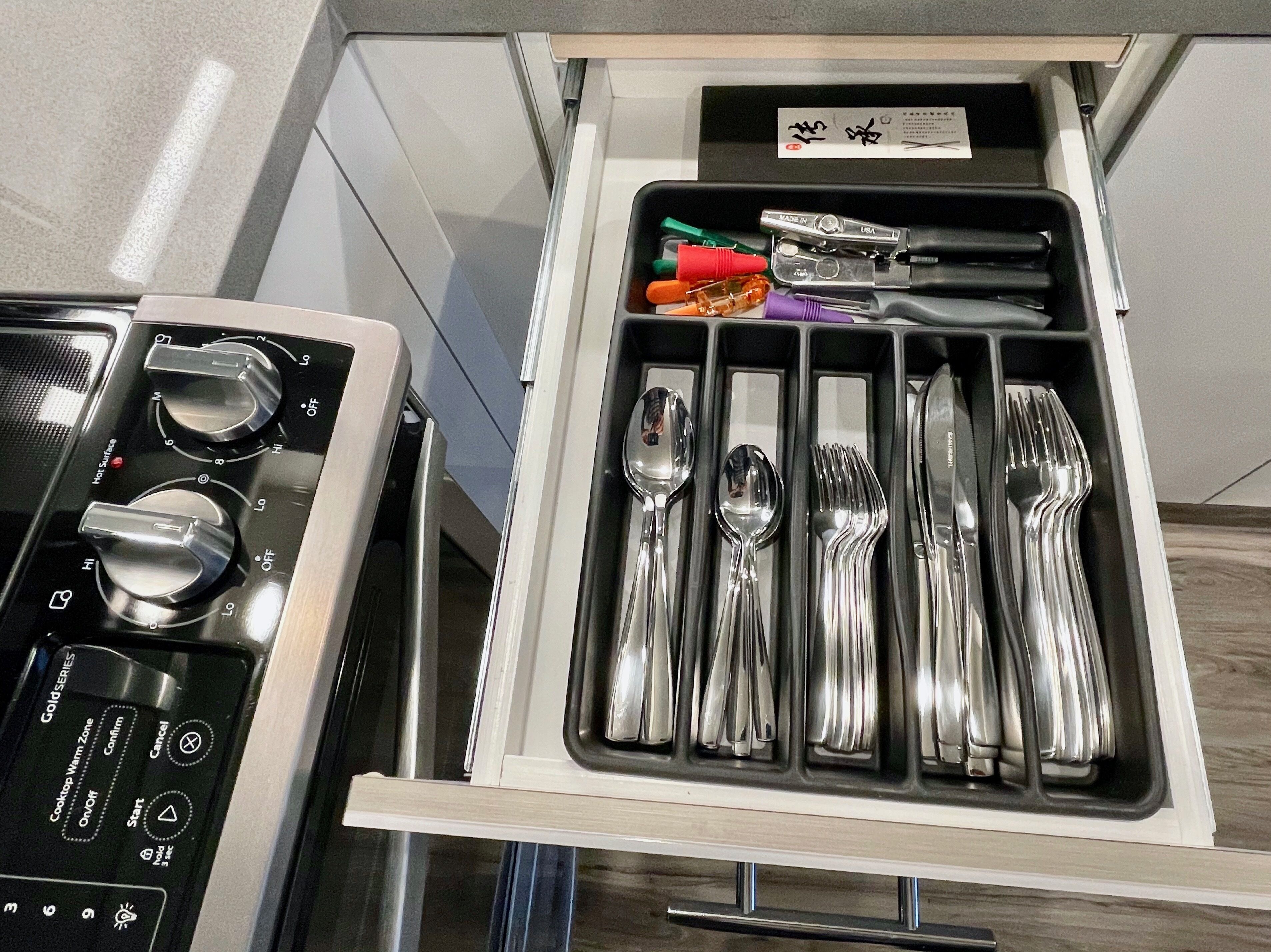 A kitchen drawer with a built-in utensil holder containing spoons, forks, and a can opener.