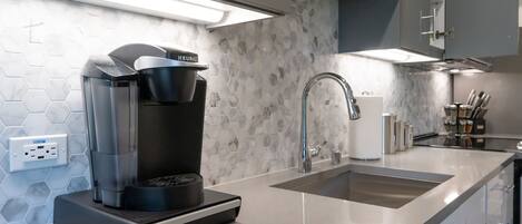 A modern kitchen with a coffee maker, a sink, and a hexagonal tile backsplash.