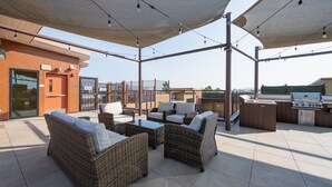 Een terras buiten met rieten meubels, een barbecue en uitzicht op de stad.