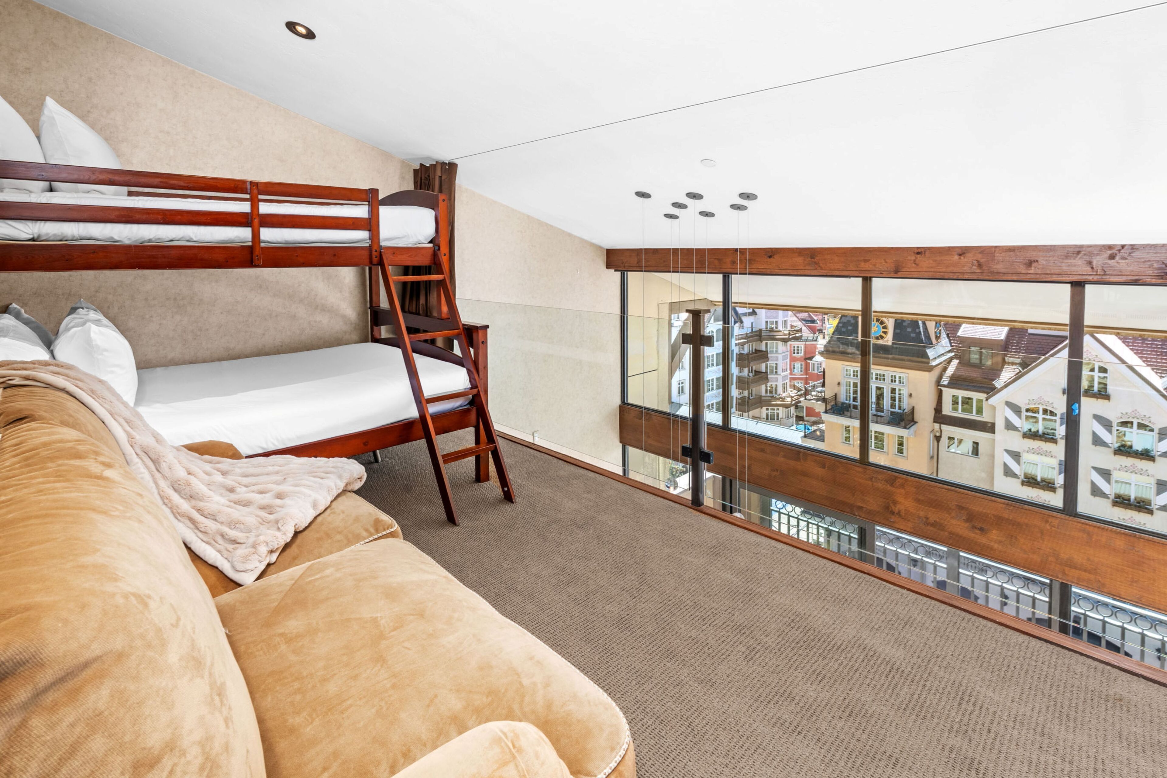 Une chambre avec un lit superposé, une échelle en bois, un canapé et une grande fenêtre donnant sur la ville.