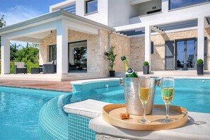 A modern pool area with a clear blue pool, a lounge chair, and a tray with a champagne bottle and glasses. - Villa Dahlia Belle with Pool (Višnjan)