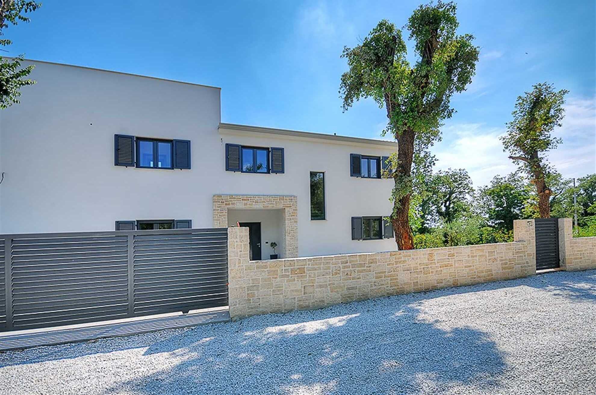 Une maison moderne à deux étages, dotée d’une façade en pierre, d’une entrée sécurisée par un portail et d’une allée gravillonnée.