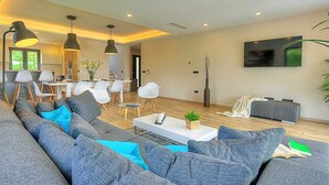 A modern living room with a large grey sofa, a coffee table, and a dining area with white chairs. - Villa Dahlia Belle with Pool (Višnjan)