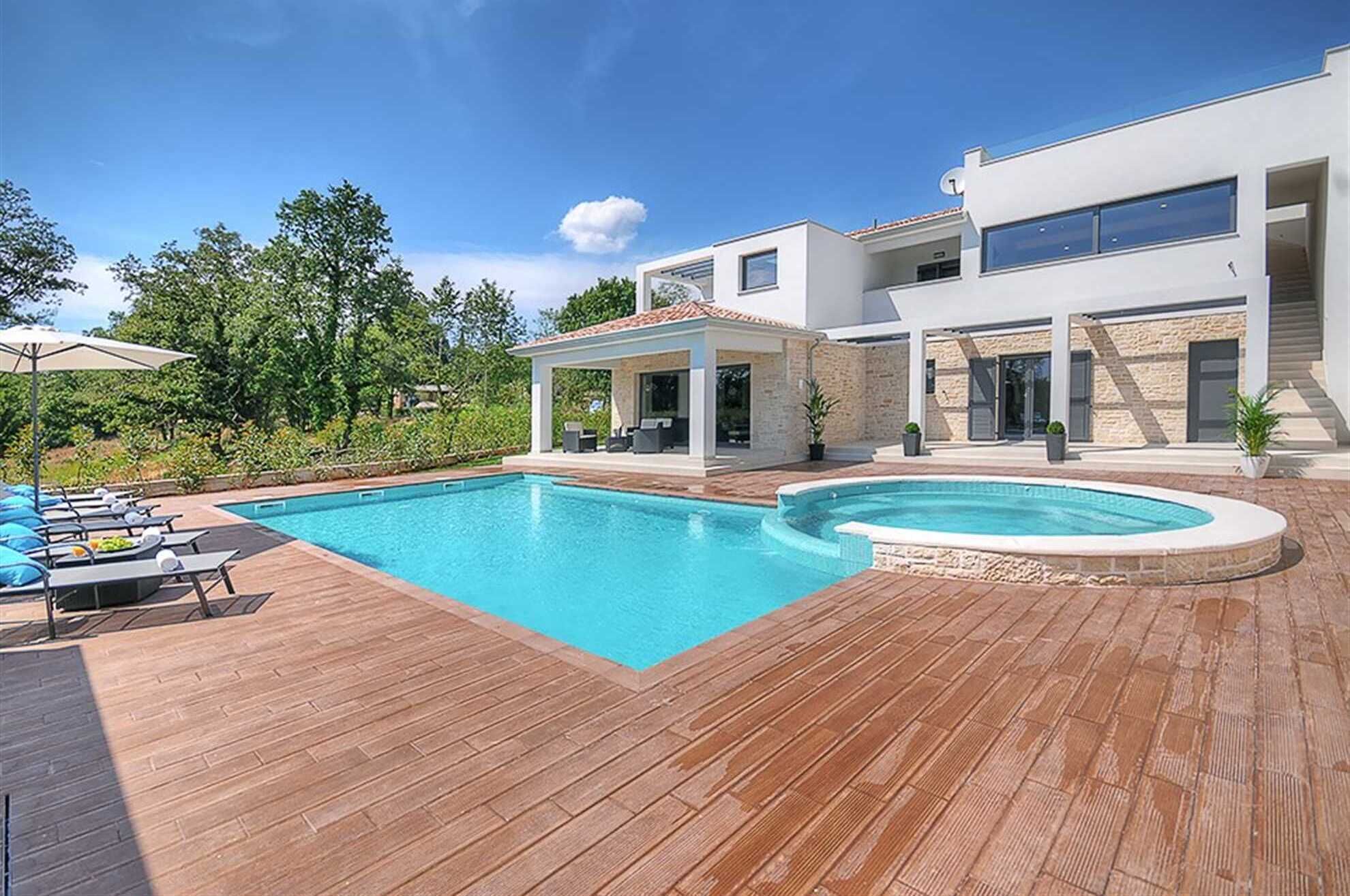 Een modern huis met een zwembad, houten terras en een zitgedeelte buiten.