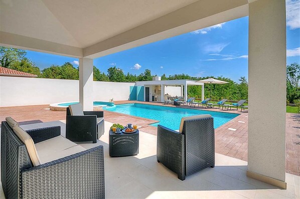 A covered outdoor area with a pool, lounge chairs, and a small table with drinks. - Villa Dahlia Belle with Pool (Višnjan)