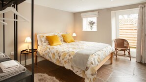 A bedroom with a bed, two bedside lamps, a chair, a window with a view of a wooden structure, and a small table with towels. - Two bedroom cottage situated in a quiet location down a secluded lane.  (Harome)