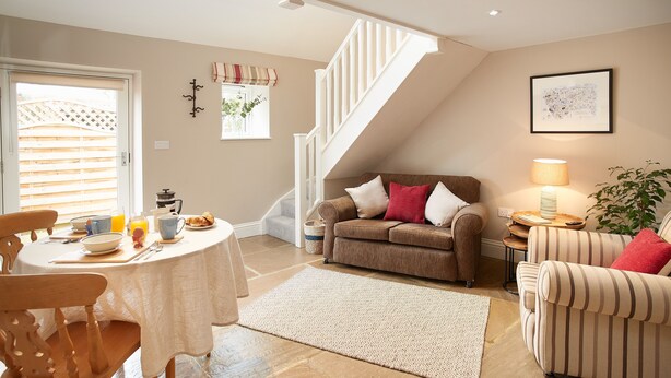 A cozy living room with a dining area, a staircase, and a dining table set with breakfast items. - Two bedroom cottage situated in a quiet location down a secluded lane.  (Harome)