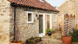 A stone building with a tiled roof, a door, and a window. There is a potted plant and a stone bench. - Two bedroom cottage situated in a quiet location down a secluded lane.  (Harome)