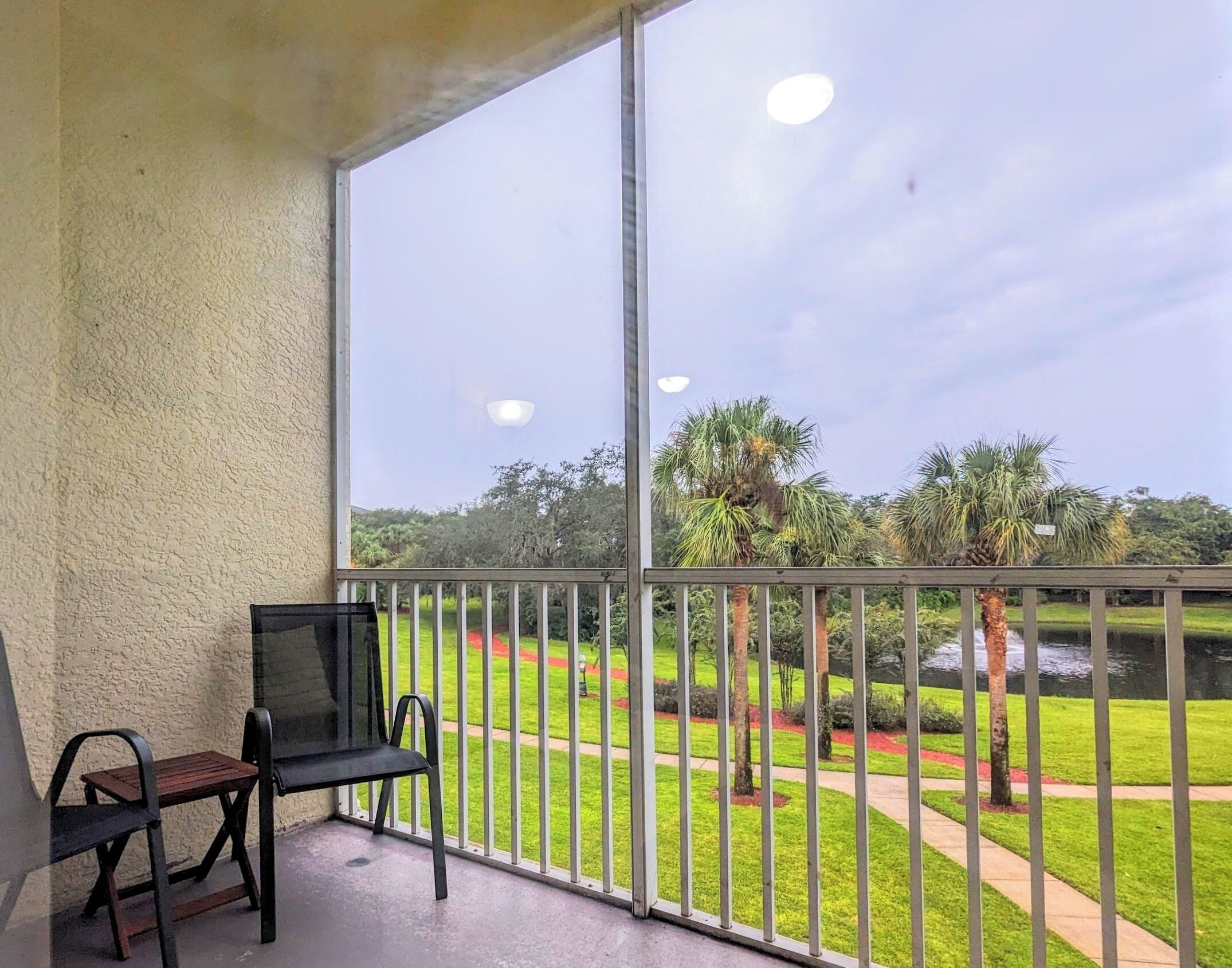 A balcony with a view of a well-maintained garden, a bench, and a table.