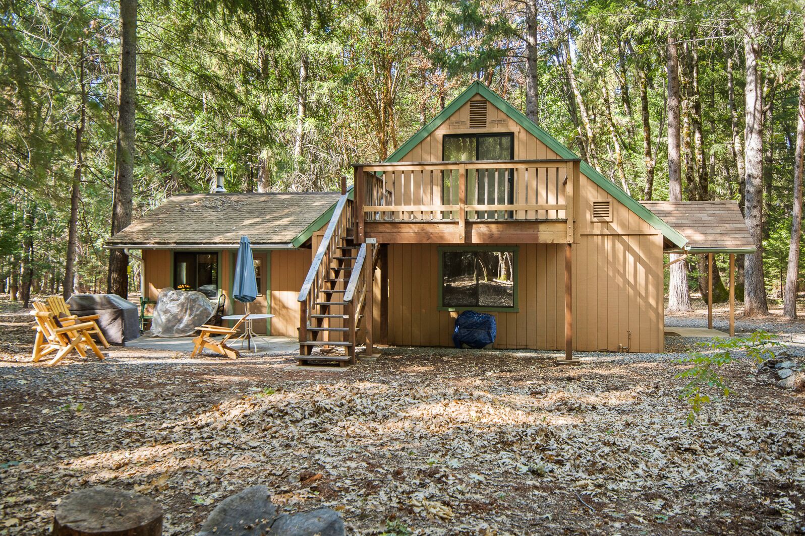A wooden cabin with a ramp and a deck, surrounded by trees.