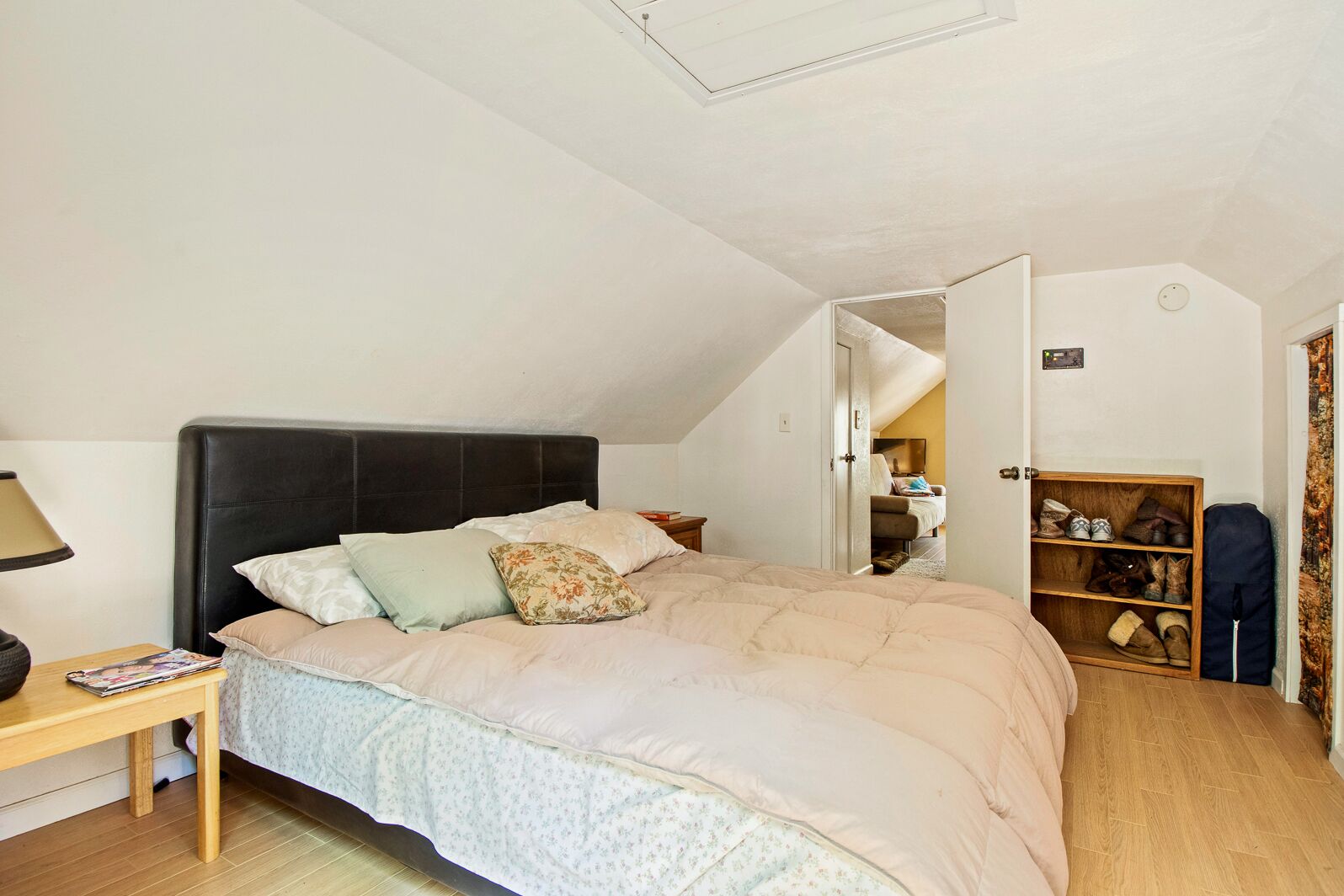 A bedroom with a bed, a nightstand, a wooden floor, a ceiling light, and a shoe rack.