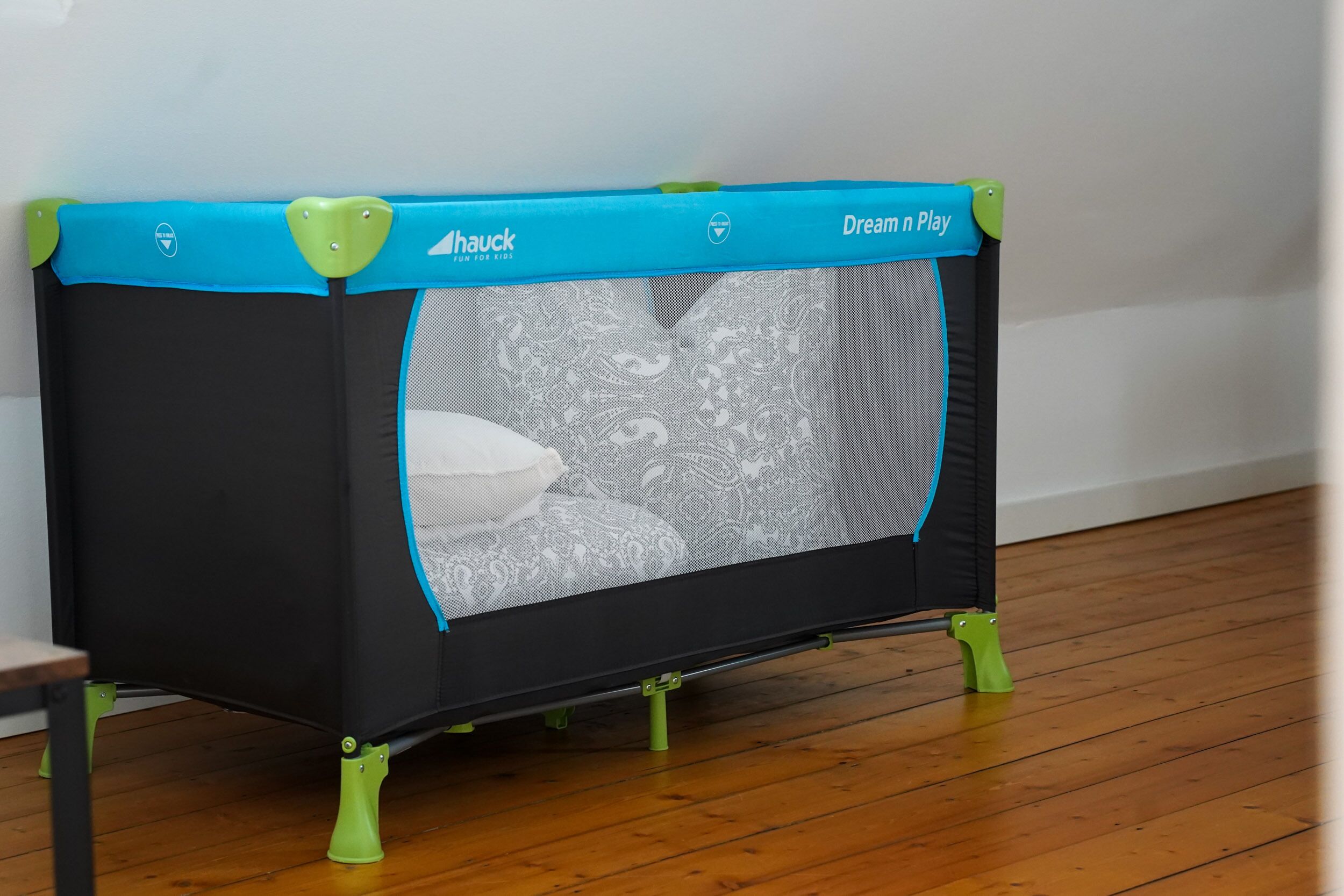 A small trampoline with a net enclosure, branded with 'Dream Play' and 'Hauck' logos, on a wooden floor.