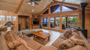 A spacious living room with a high ceiling, wooden walls, a large sofa set, a wooden coffee table, and a fireplace. - Serene Lakeside Getaway (Pittsburg)
