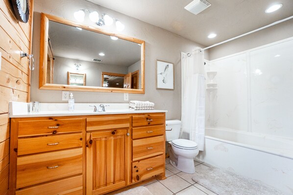 A bathroom with wooden cabinetry, a large mirror, a toilet, and a shower area.
