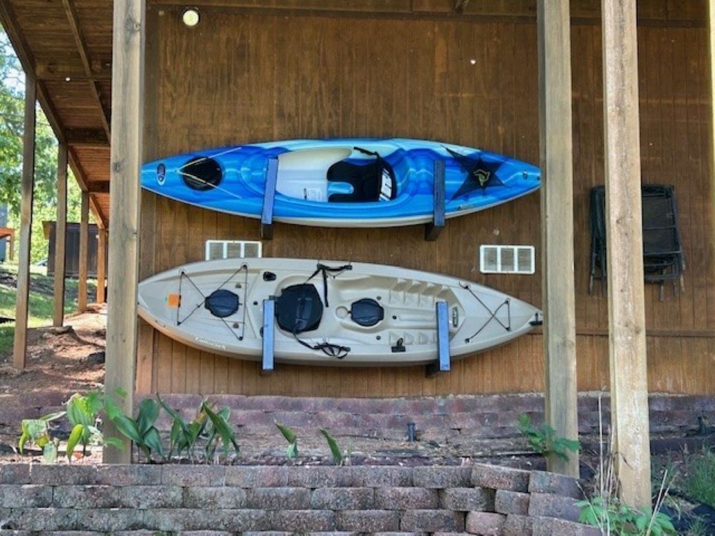 Two kayaks mounted on a wooden wall under a covered area.