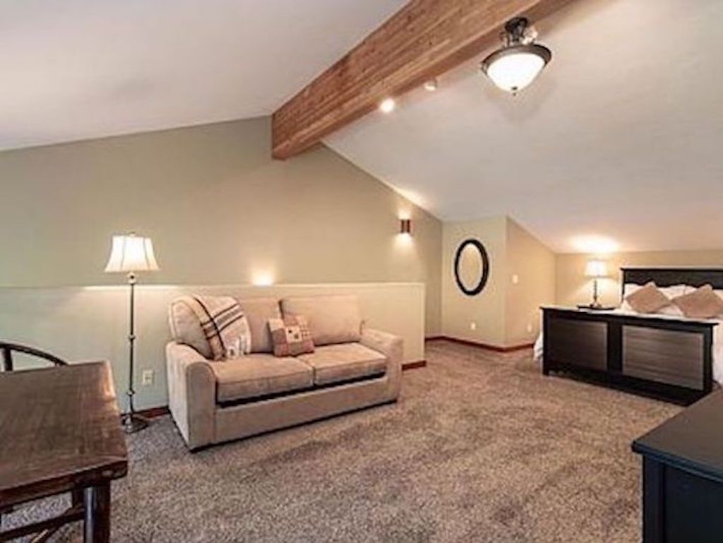 A cozy loft bedroom with a high ceiling, a bed, a nightstand, a lamp, and a sofa.