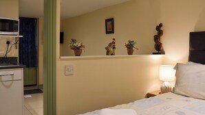 Una habitación de hotel con cama, lámpara de noche, microondas y estante con objetos decorativos.