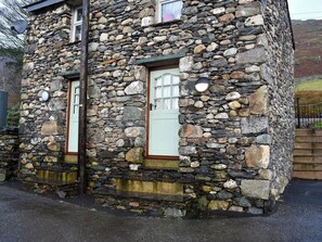 A stone building with two windows and a door, featuring a rustic stone exterior and a small porch area.