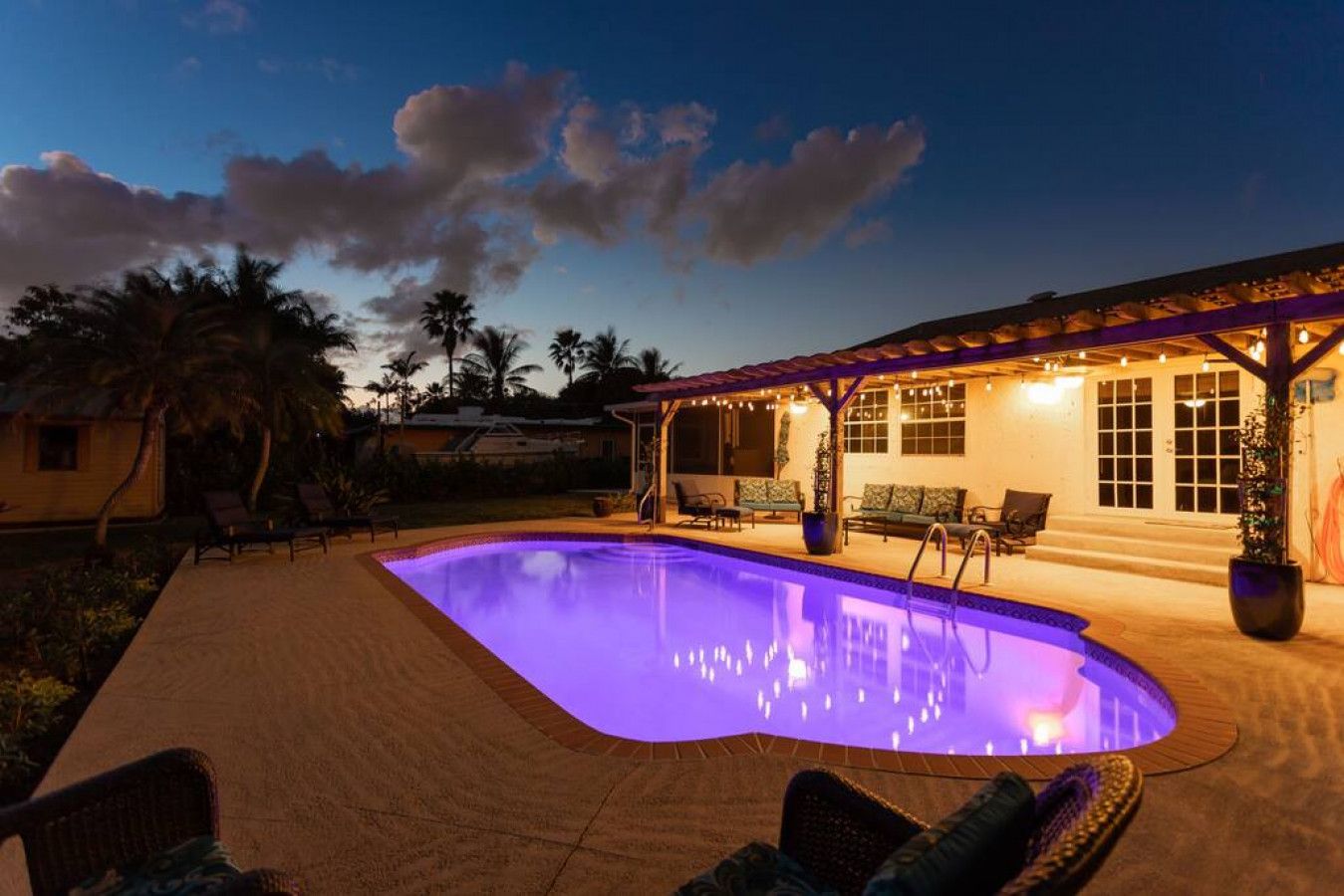 Une piscine avec un espace patio, des chaises longues et un coin salon couvert offrant une vue sur la piscine.