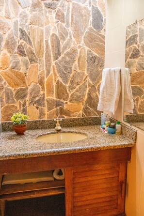 Une salle de bain avec un mur en pierre, un comptoir en granit, un lavabo, un miroir et un porte-serviettes.