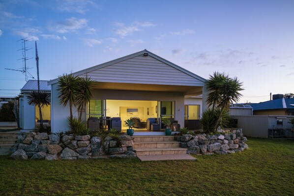 Una casa moderna amb un porxo cobert, escales de pedra i un jardí daurat.