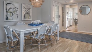 A dining area with a white table, wicker chairs, and a chandelier. There are abstract paintings on the wall and a mirror on the right. - 3BR End Unit Spinnaker w/ Beach Boardwalk Access Across Street! Amenity access included! NO pets (Seabrook Island)