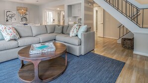 A modern living room with a sectional sofa, a wooden coffee table, and a herringbone-patterned rug. A staircase with a metal railing leads to an upper level. - 3BR End Unit Spinnaker w/ Beach Boardwalk Access Across Street! Amenity access included! NO pets (Seabrook Island)