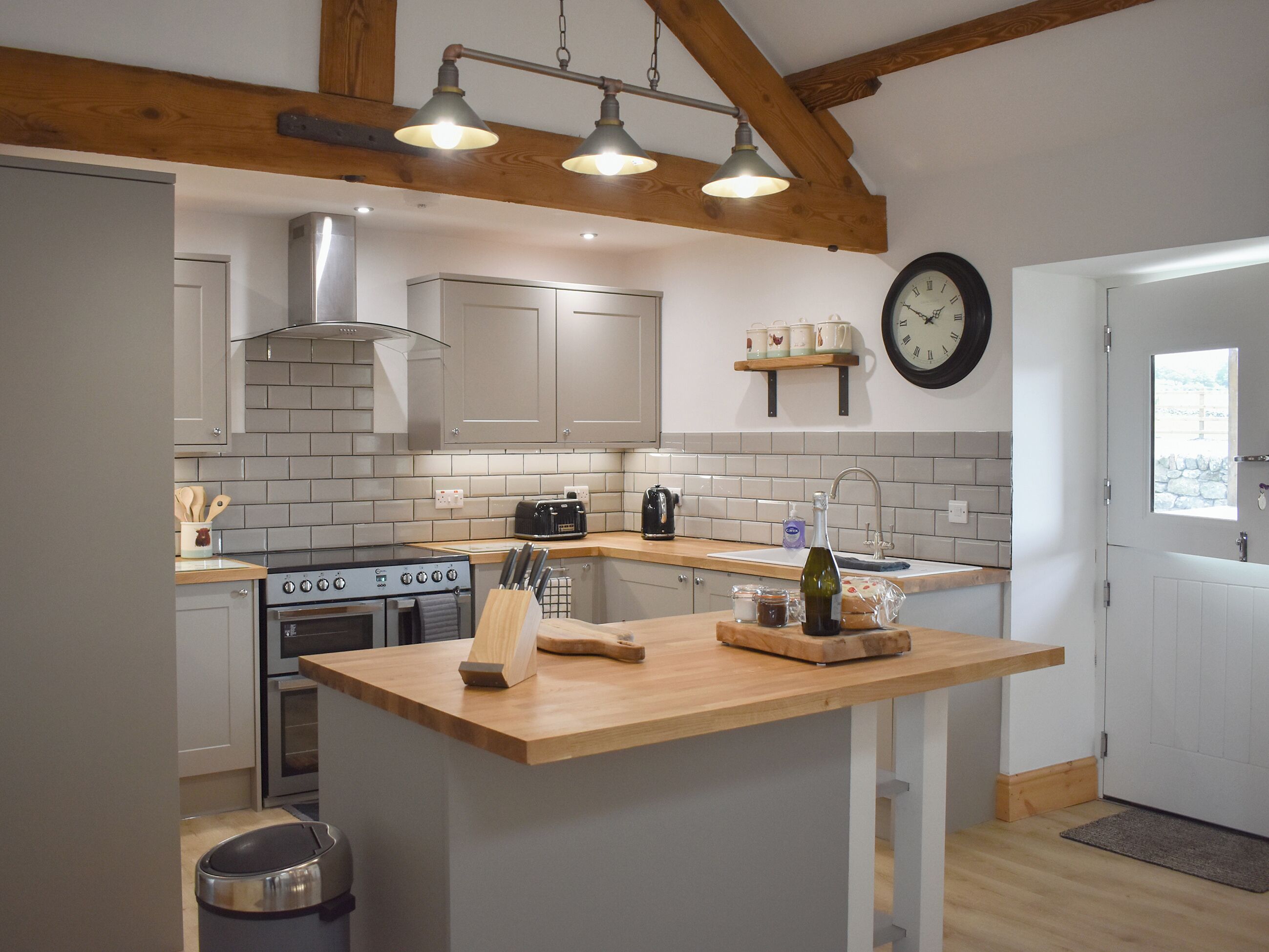 Een moderne keuken met een centraal eiland, een ingebouwde oven en een klok aan de muur.