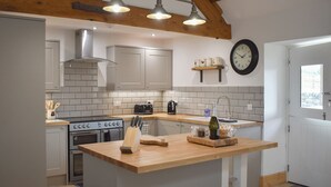 A modern kitchen with a central island, a built-in oven, and a clock on the wall. - 3 bedroom accommodation in Penygroes, Caernarfon (Penygroes, Caernarfon)