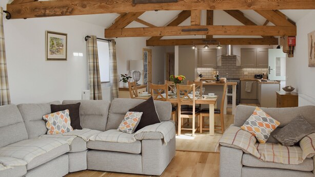 A spacious living room with a large sectional sofa, a dining area, and a kitchen in the background. - 3 bedroom accommodation in Penygroes, Caernarfon (Penygroes, Caernarfon)