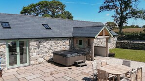 A stone building with a patio area, including a hot tub, a table with chairs, and a stone wall. - 3 bedroom accommodation in Penygroes, Caernarfon (Penygroes, Caernarfon)