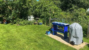 A backyard with a blue table and a covered grill, surrounded by greenery and potted plants.