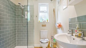 A bathroom with a glass shower enclosure, a toilet with a decorative cover, a sink with a mirror, and a window with a view of the outside. - 1 bedroom accommodation in Booton, Reepham (Booton, Reepham)