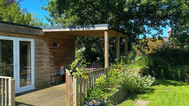 A wooden deck with a pergola, potted plants, and a grassy garden area. - 1 bedroom accommodation in Booton, Reepham (Booton, Reepham)