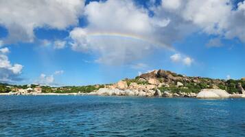A coastal landscape with a rainbow, clear sky, and rocky terrain.