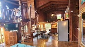 Un intérieur spacieux en bois, avec un plafond haut, un escalier, un coin repas et une cuisine.
