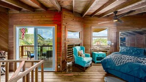 L’intérieur d’un chalet en bois, avec un lit, un fauteuil bleu, une petite table et une bibliothèque.