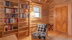 Ein gemütliches Holzblockhaus-Interieur mit Holzregalen, einem Lesesessel, einem Fenster und einer Tür.