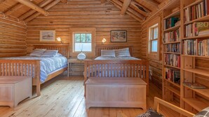 Ein Schlafzimmer in einer Blockhütte mit zwei Betten, einem Bücherregal und einem Fenster.