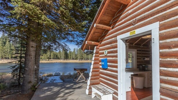 Eine Blockhütte mit einer Holzterrasse, einer Bank und Blick auf einen See.